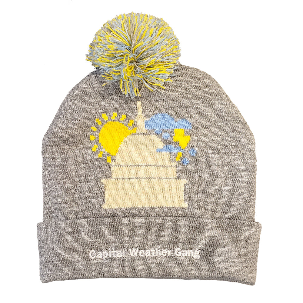grey beanie with blue and yellow pompom and capital building with a yellow sun and lightning raincloud surrounding it. capital weather gang inscribed on headband portion of hat