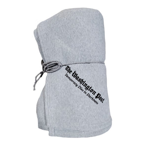 Light gray sweatshirt blanket rolled up and tied with light gray drawstring. The Washington Post and Democracy Dies in Darkess is stitched in black text on a diagonal angle in the bottom corner.