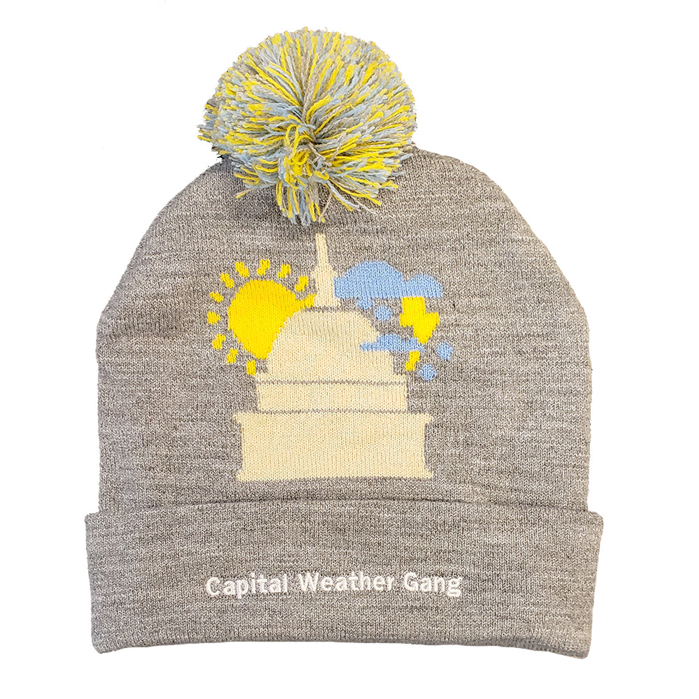 grey beanie with blue and yellow pompom and capital building with a yellow sun and lightning raincloud surrounding it. capital weather gang inscribed on headband portion of hat 