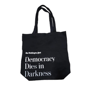 Black canvas tote bag with The Washington Post in small white text and Democracy Dies in Darkness in large white text below it.
