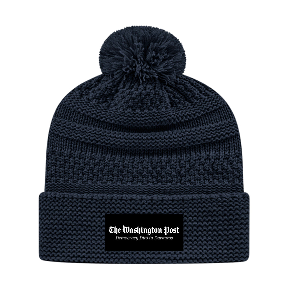 Navy blue knitted winter hat with pompom on the top. Black tag with The Washington Post Democracy Dies in Darkness in white on the front brim.